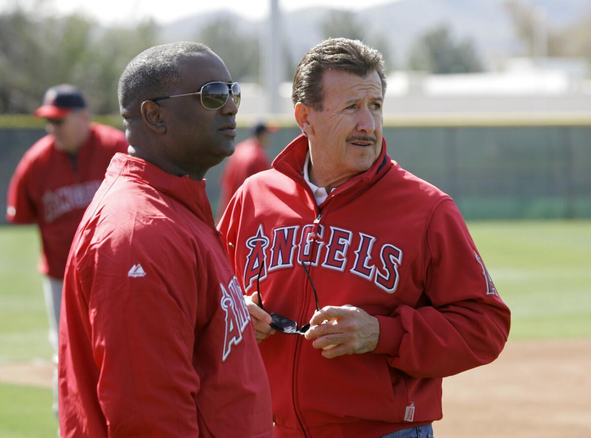Angels general manager Tony Reagins, left, stands on a baseball field talking to team owner Arte Moreno