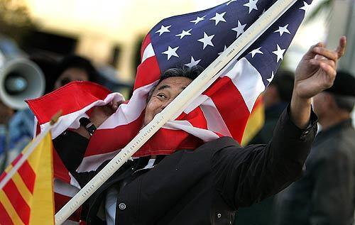 A protester with American and South Vietnamese flags shouts a chant in the parking lot outside the offices of the Nguoi Viet newspaper in Westminster. The paper printed a photo of an artwork that some in Little Saigon say is insulting to the flag of the former South Vietnam.