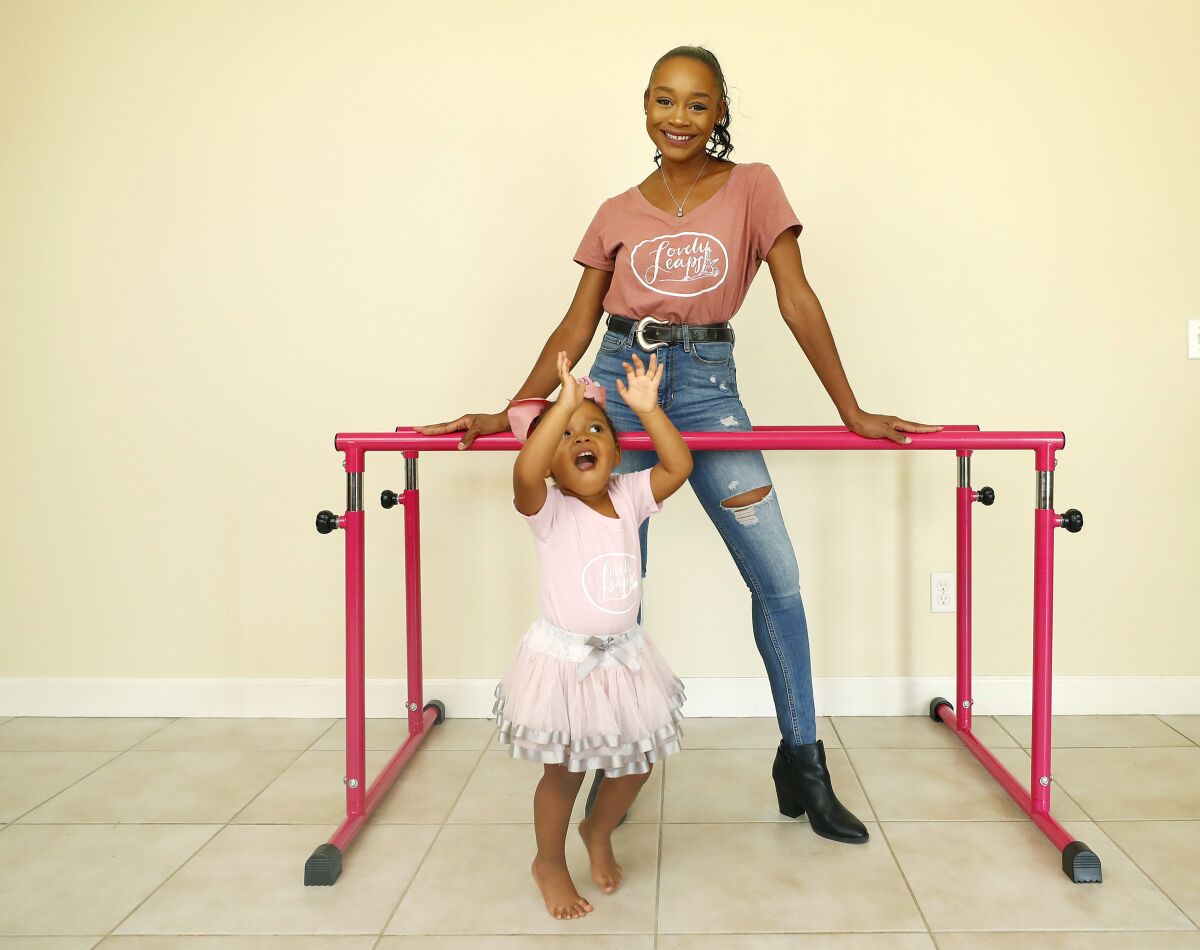 Lisa McCabe stands at a ballet barre, smiling. Her 2-year-old daughter dances in front of her in a tutu. 