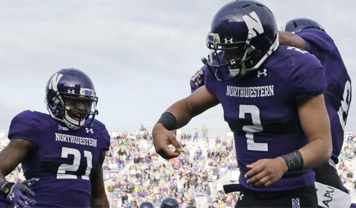 Northwestern quarterback Kain Colter, shown celebrating a touchdown with running back Stephen Buckley (8) and wide receiver Kyle Prater (21), marked the letters "APU" on his wristbands and towel as part of an organized demonstration.