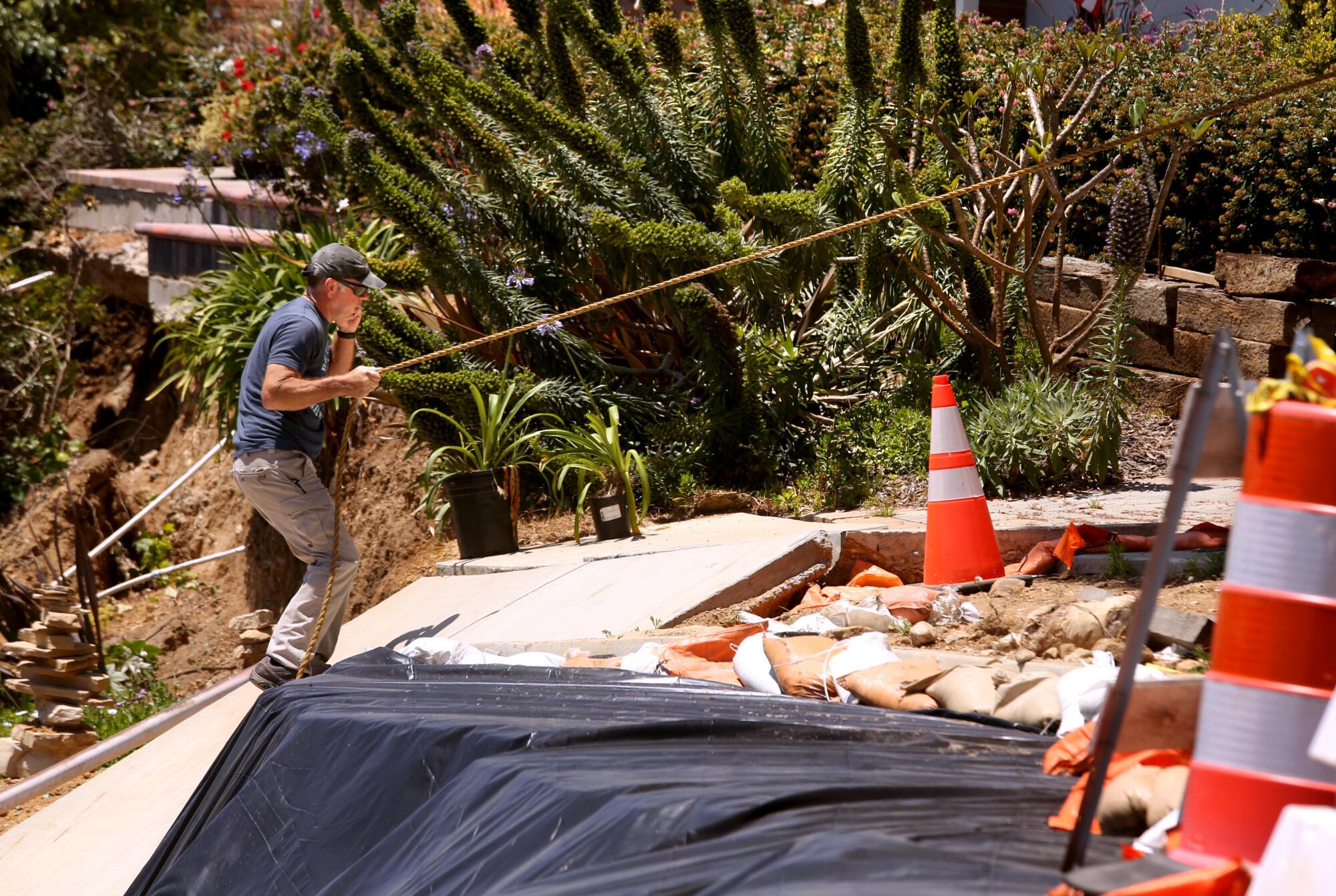 A man uses a rope line for support as he crosses a damaged driveway.