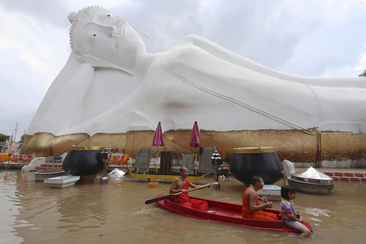 Buddhist monks paddle a boat through floodwaters in front of a reclining Buddha at the Wat Satue in Ayutthaya province north of Bangkok, Thailand, Monday, Oct. 4, 2021. Officials in Thailand expressed optimism Monday that widespread flooding is easing, with signs that the capital, Bangkok, may be spared serious damage. (AP Photo/Nathathida Adireksarn)