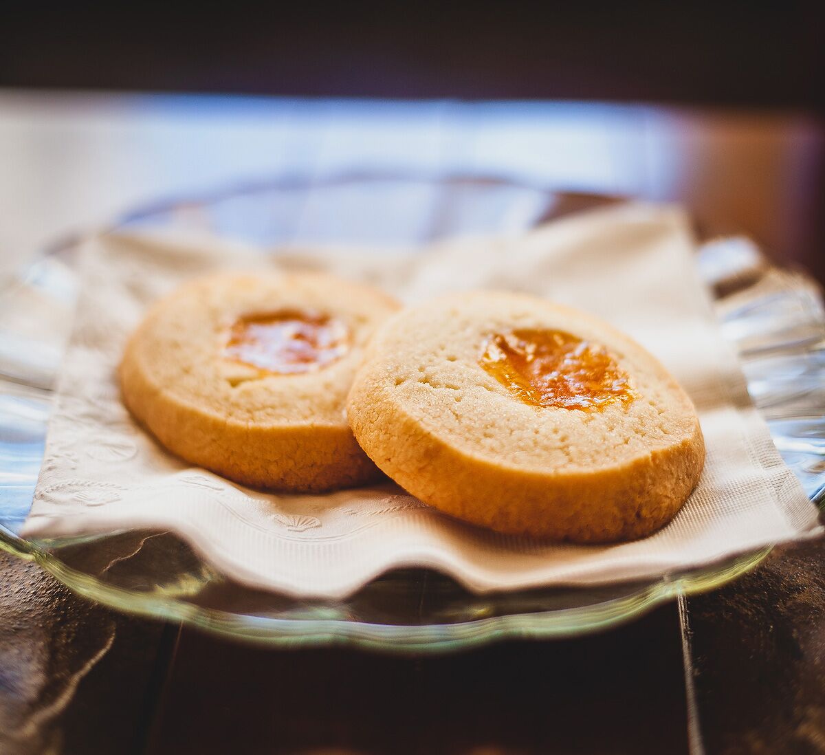 Two apricot preserve thumbprint cookies on a plate.
