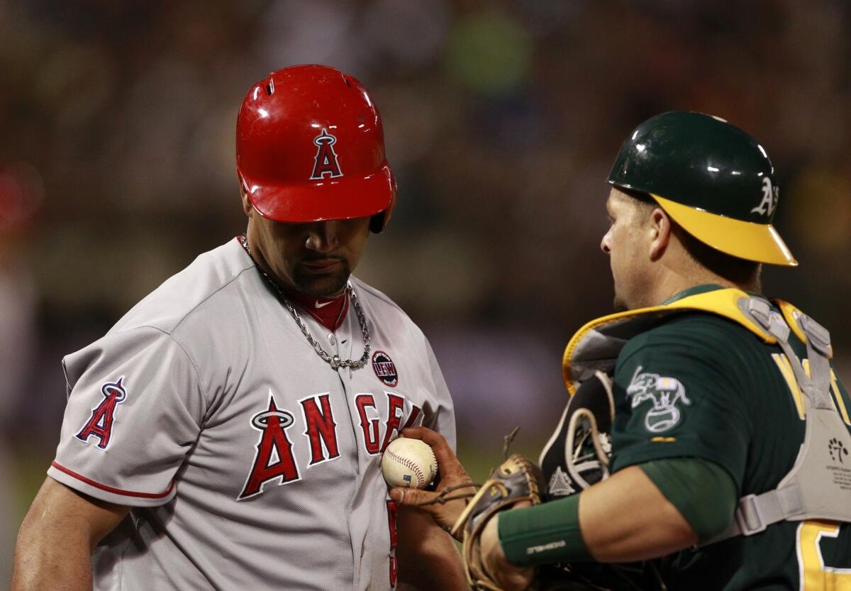 Angels slugger Albert Pujols, left, is tagged out by Oakland Athletics catcher Stephen Vogt during a game in July. Pujols will miss the rest of the season because of a lingering foot injury.