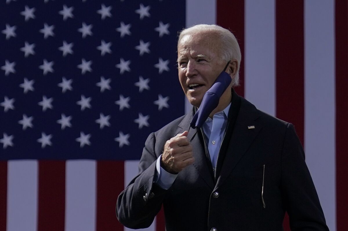 Former Vice President Joe Biden removes his face mask in front of a flag backdrop onstage in Durham, N.C.