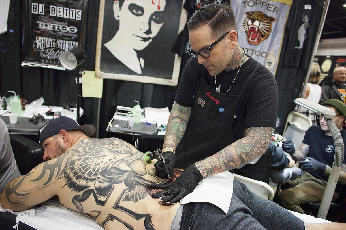 Artist Dan Smith, with Captured Tattoo in Tustin, tattoos a tiger head on the back of Derick Durbin, of West Covina, during the 9th annual Musink Tattoo Convention and Music Festival at the OC Fair & Event Center in Costa Mesa on Friday.