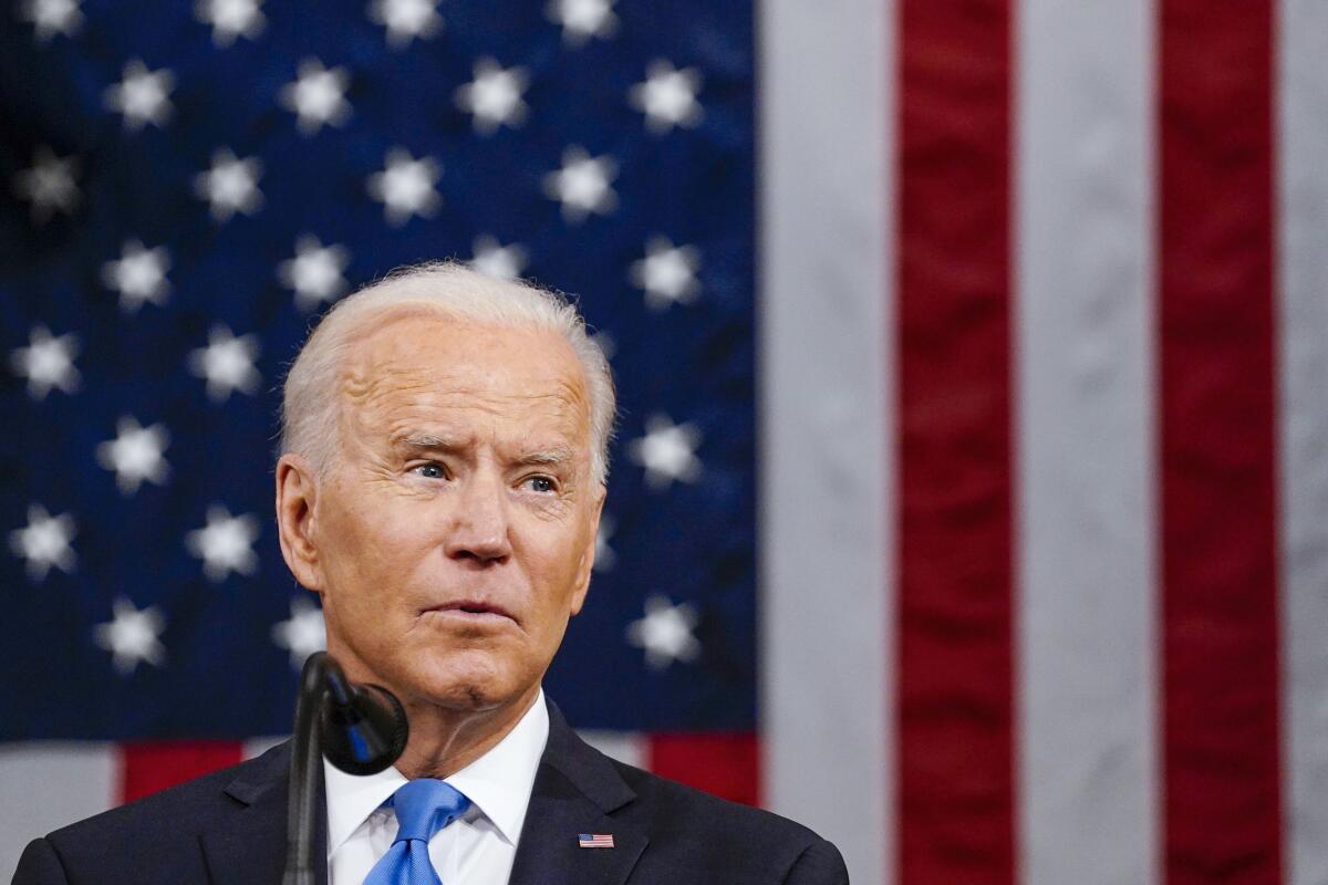 Joe Biden looks to his left at a microphone with the American flag as a backdrop 