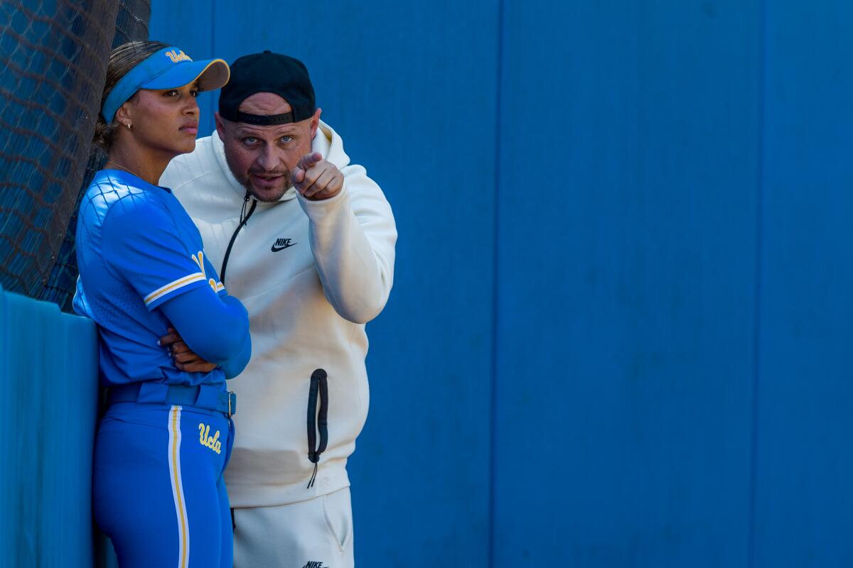 UCLA mental wellness coach Armando Gonzalez speaks with senior Maya Brady while stand on a softball field.