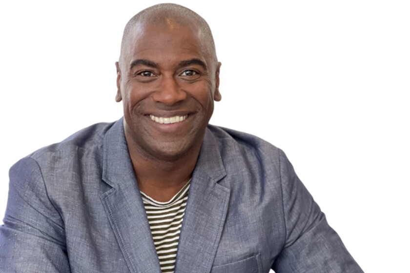 A man smiles wearing a striped shirt and a chambray blazer.