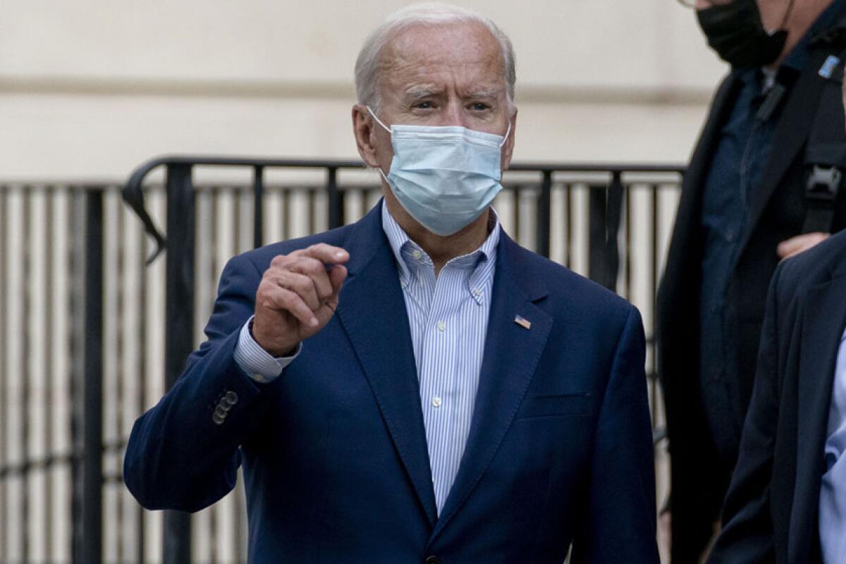 President Biden, in blue suit and face mask, answers questions outdoors