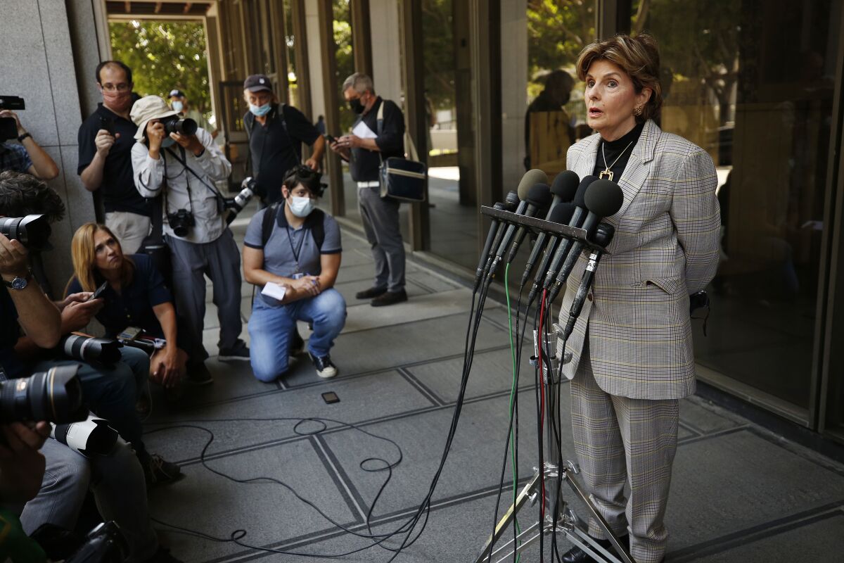 A woman speaks behind multiple microphones as media members watch