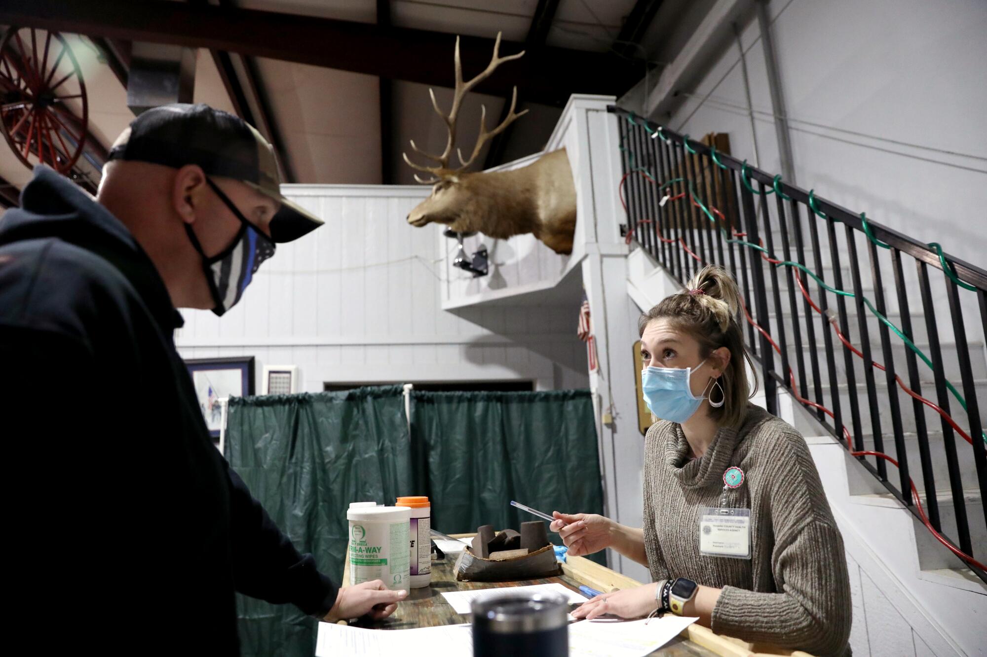 A man in a mask checks in a desk with a woman seated behind it