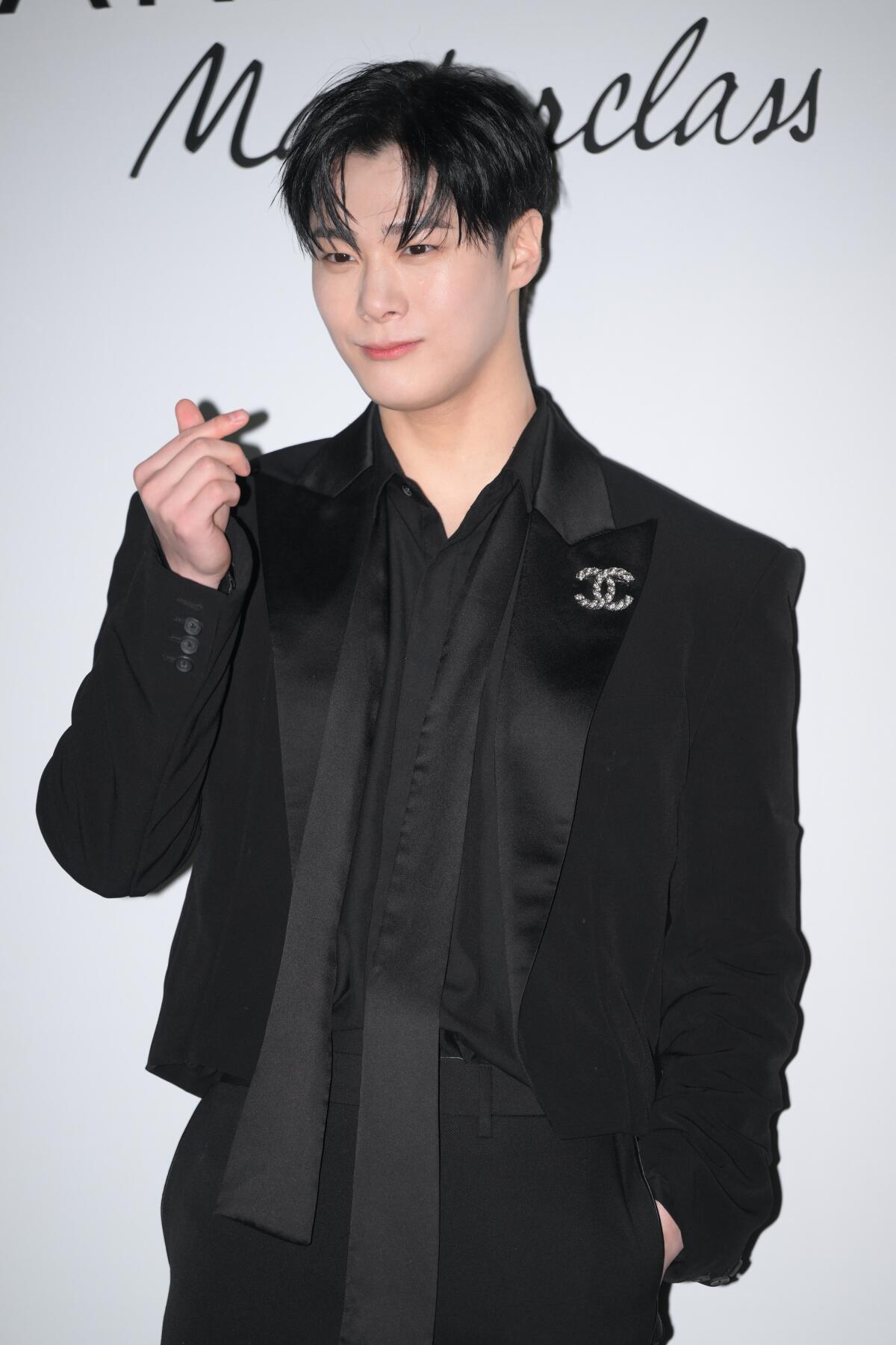 Moon Bin of K-pop group Astro poses in a black suit with one hand in his pocket and the other near his shoulder