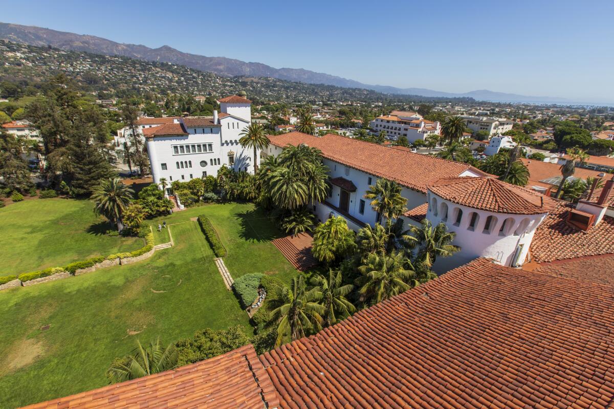 A white Spanish-style building with red tile roof and green courtyard, seen from above in an aerial shot