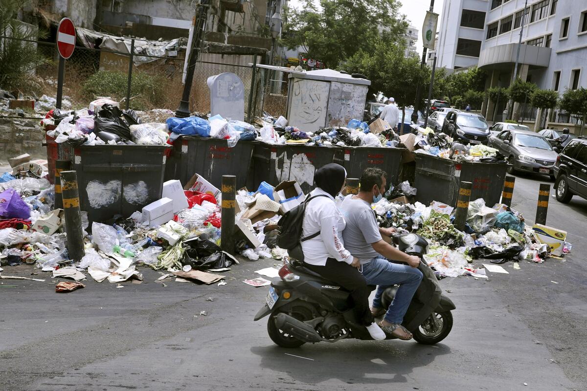 People on a scooter passing piled-up garbage on a Beirut street