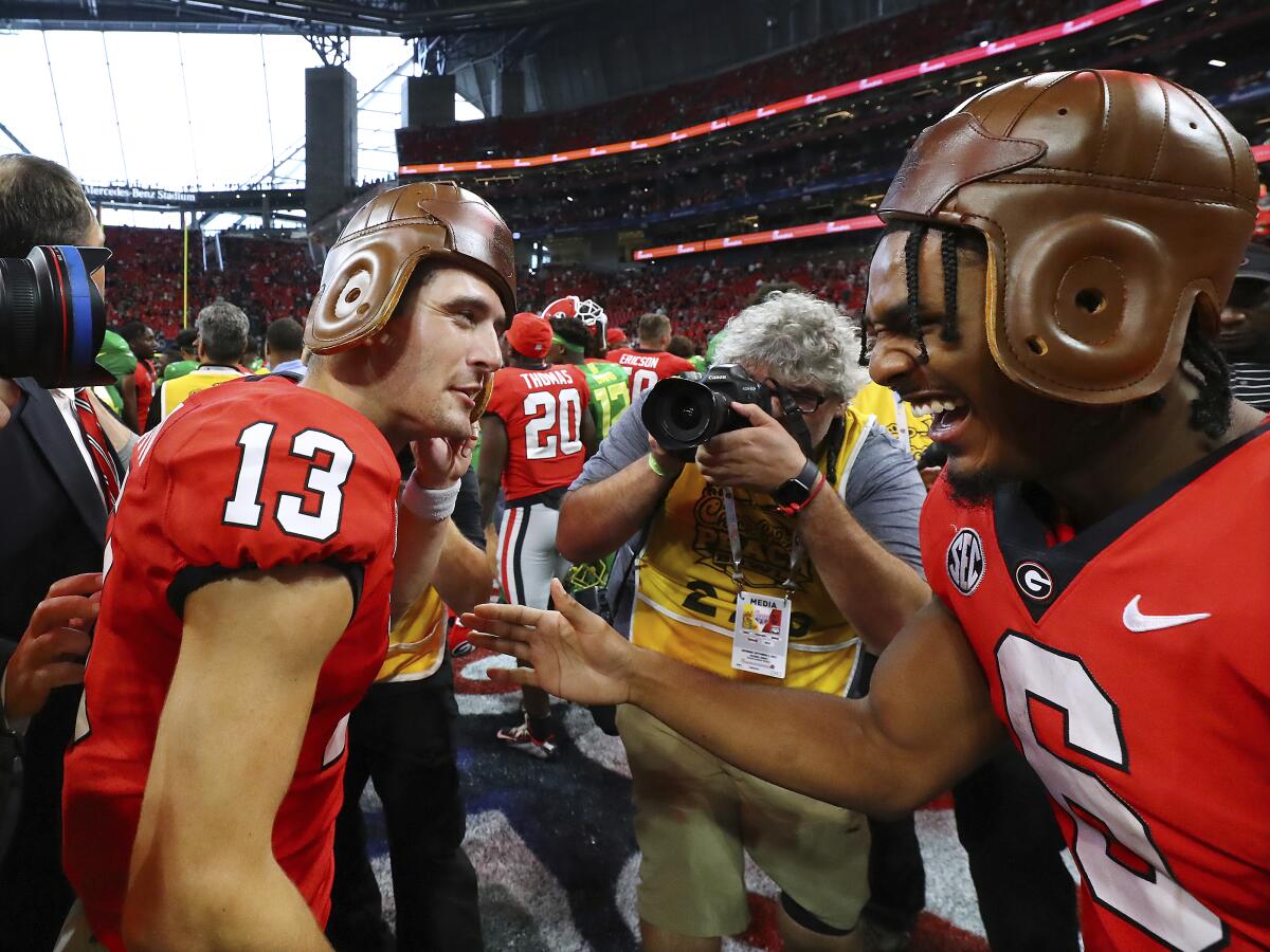 Georgia quarterback Stetson Bennett and running back Kenny McIntosh put on old leather helmets while celebrating a 49-3 victory over Oregon in an NCAA college football game on Saturday, Sept. 3, 2022, in Atlanta. (Curtis Compton/Atlanta Journal-Constitution via AP)