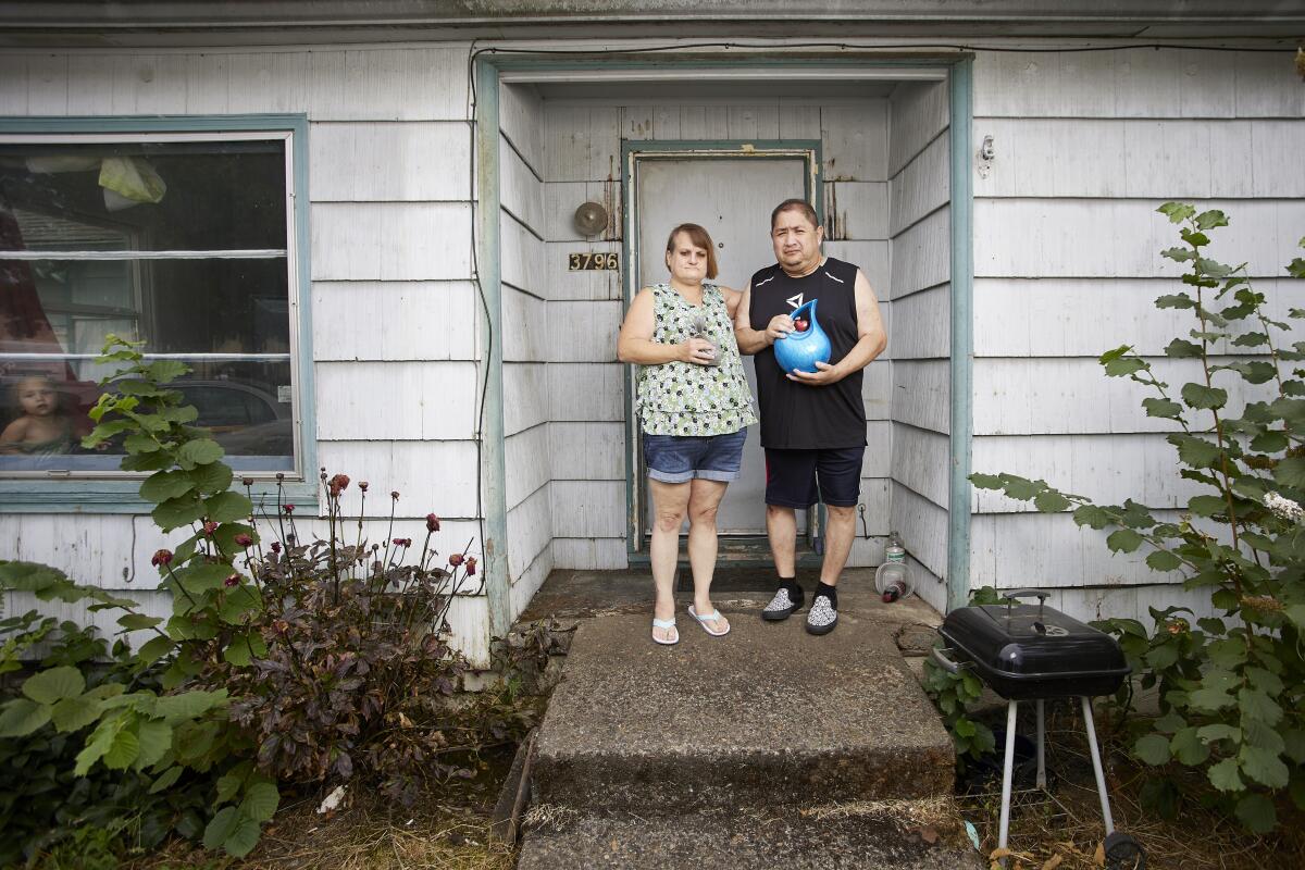 A couple stands in front of their home, holding the urn containing the ashes of their son.