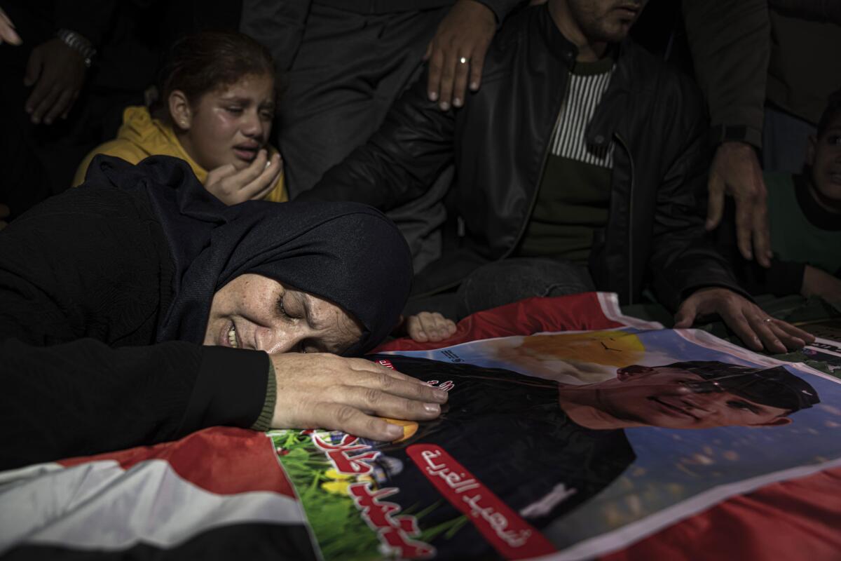 A woman lays her head on a flag-draped coffin while others watch.