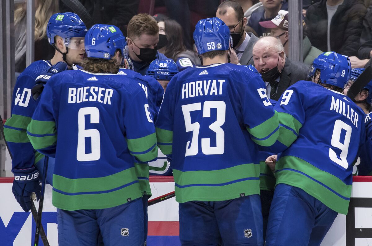 Vancouver Canucks head coach Bruce Boudreau, back right, talks to Elias Pettersson, of Sweden, from left to right, Brock Boeser, Bo Horvat and J.T. Miller during a timeout during the third period of an NHL hockey game against the Columbus Blue Jackets Tuesday, Dec. 14, 2021 in Vancouver, British Columbia. (Darryl Dyck/The Canadian Press via AP)