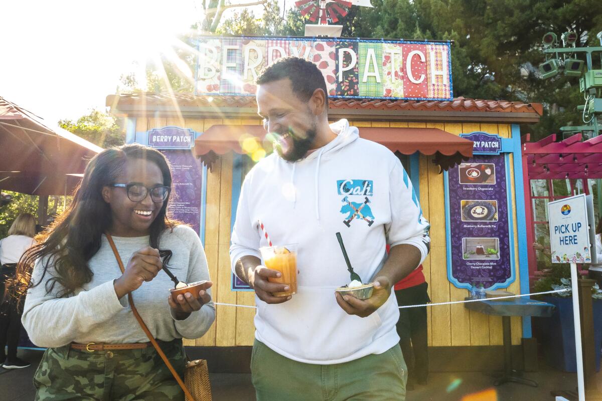 Two people hold small trays of food and a drink while visiting Disney California Adventure Food & Wine Festival 