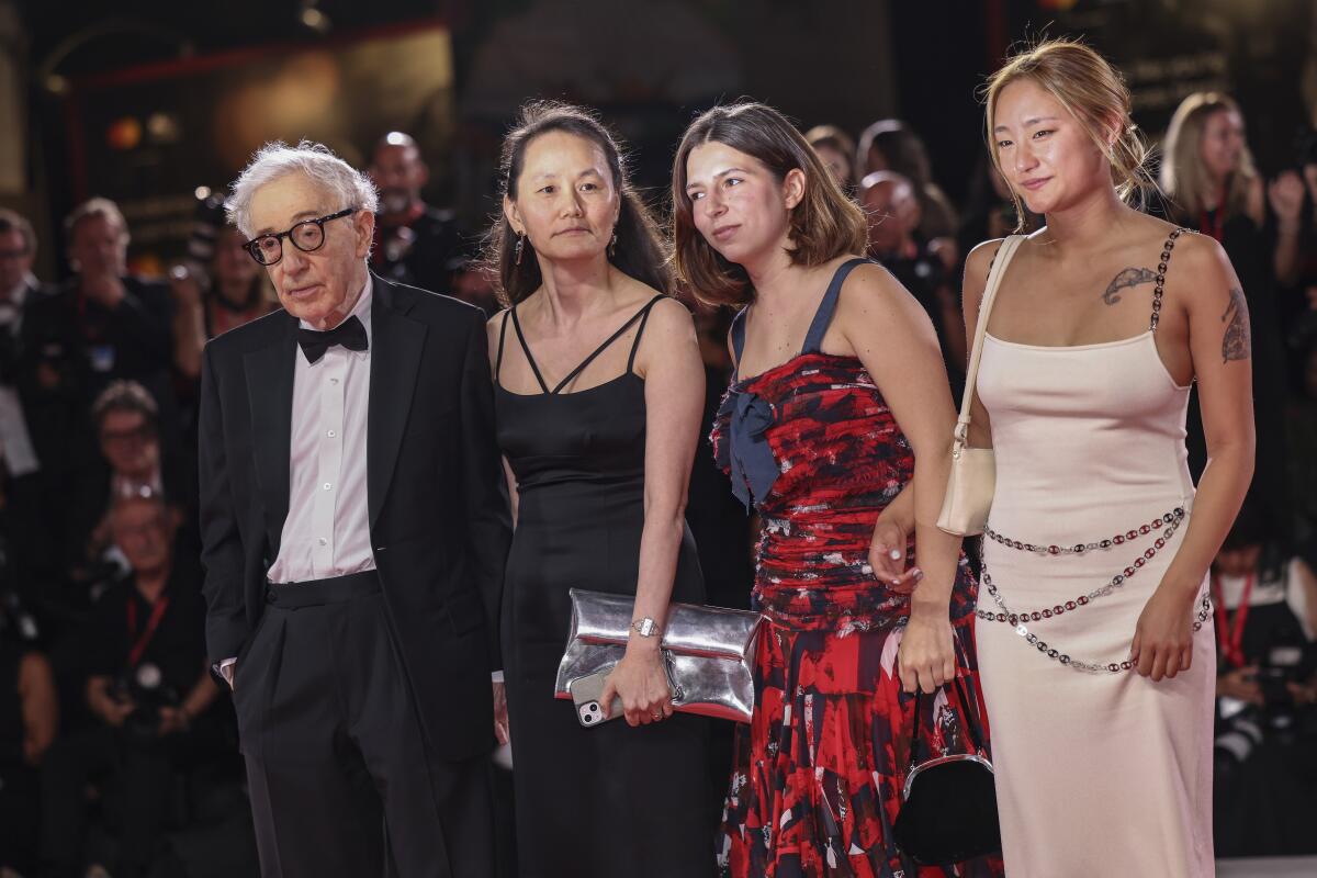 Woody Allen in a tuxedo poses next to three women in gowns.