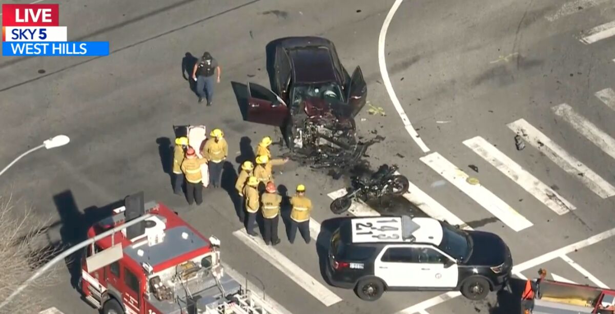 Firefighters and police next to the wreckage of a car and a motorcycle in an intersection