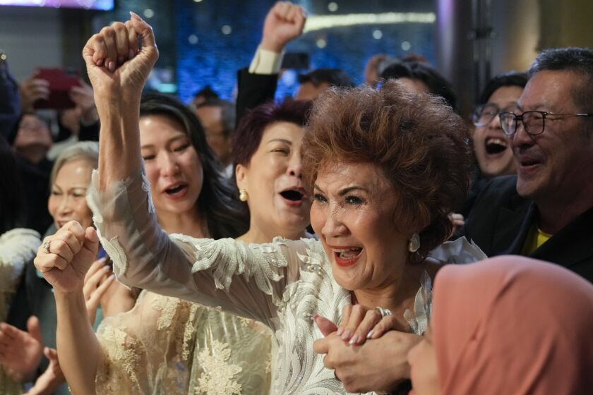 Woman, Janet Yeoh, mother of Michelle Yeoh, celebrates her daughter's Oscars win with a raised fist amid cheering crowd 