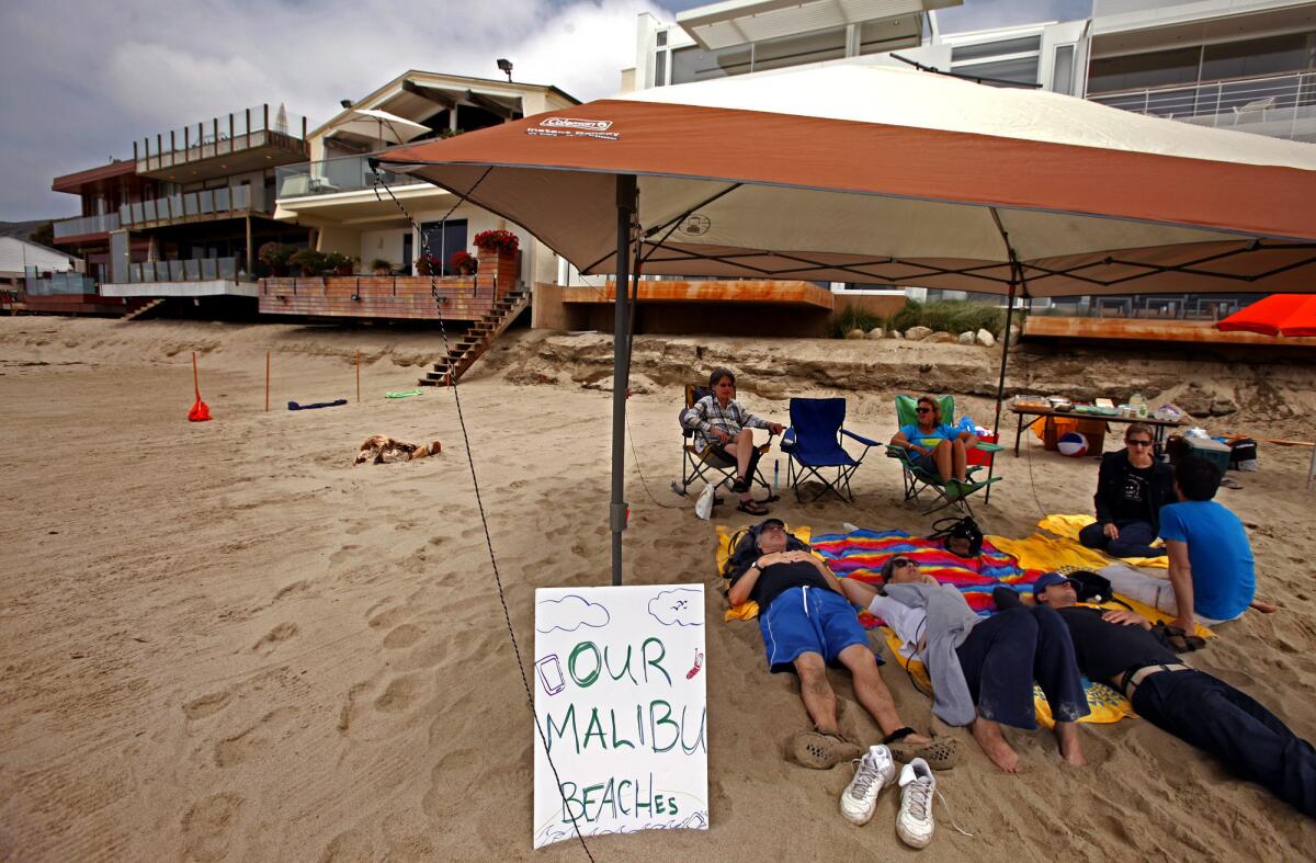 Jenny Price, seated in chair, left, and Ben Adair, wearing a blue T-shirt, are joined by friends on a stretch of beach in Malibu.
