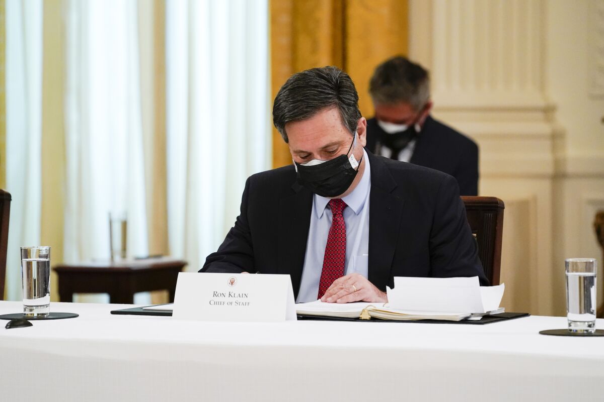 A man sits at a desk while wearing a mask and looking through papers.
