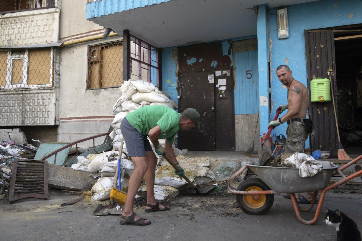 ARCHIVO - Viktor Lazar, a la derecha, limpia la calle ante su apartamento en el distrito de Saltivka 