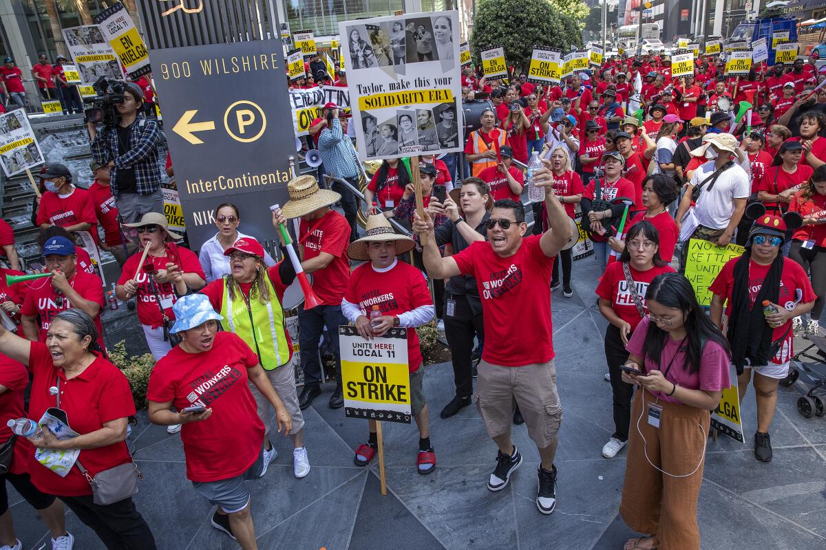 Workers gather in red shirts and signs to strike outside a hotel.
