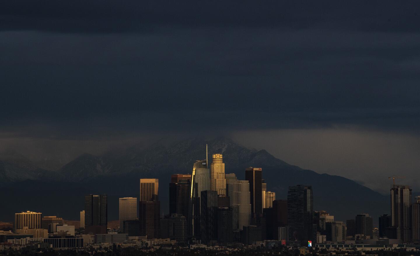 The setting sun peeks through a cloud layer, illuminating downtown skyscrapers as the season’s first storm moves through the basin and brings rain in Los Angeles.