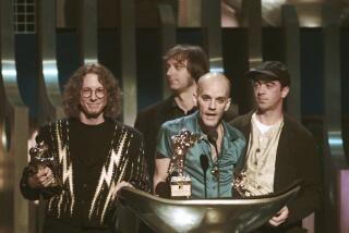The four members of R.E.M stand behind a podium holding trophies at the 1995 MTV Video Music Awards