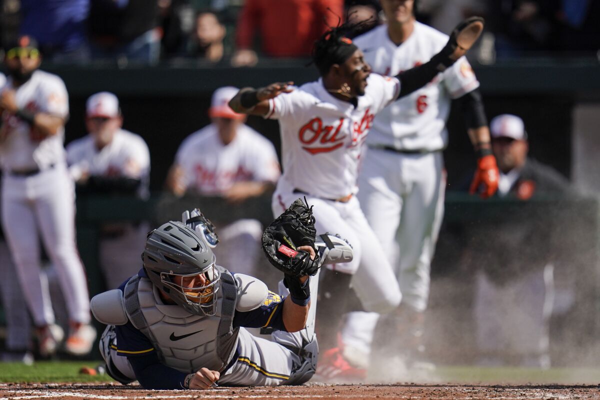 Milwaukee Brewers catcher Victor Caratini, left, holds up the ball after missing the tag on Baltimore Orioles' Jorge Mateo, back, who scores on a single by Jorge Mateo during the second inning of a baseball game at Oriole Park at Camden Yards, Monday, April 11, 2022, in Baltimore. (AP Photo/Julio Cortez)