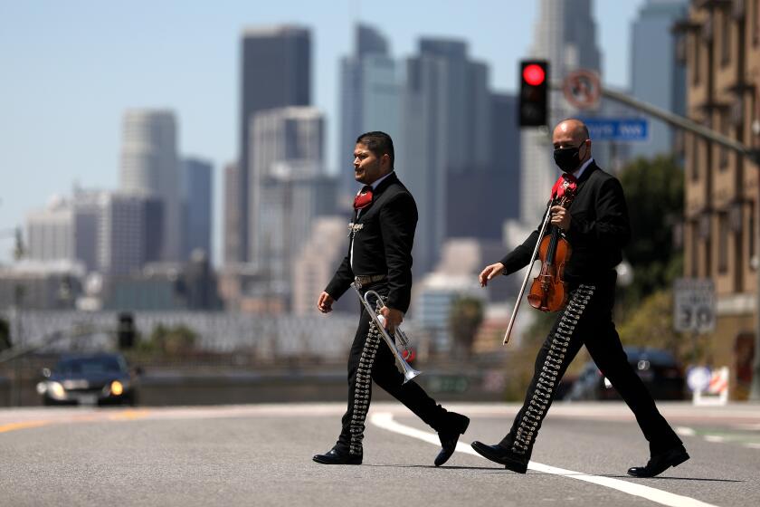 LOS ANGELES, CA -- APRIL 15: Alejandro Bustos, left, walks across First Street, after joining other Mariachi musicians in solidarity asking Los Angeles County officials for economic help during the coronavirus pandemic at Mariachi Plaza in Boyle Heights on Wednesday, April 15, 2020, in Los Angeles, CA. Mariachi musicians from various groups join in solidarity asking Mayor Eric Garcetti and Los Angeles Councilman Jose Huizar for economic support during the coronavirus pandemic. The musicians have been out of work for six weeks and are asking for support to help pay rent, bills and money to help support their families. Many of the musicians are contracted by the public to play at birthday parties, weddings, at restaurants and quincianeras. (Gary Coronado / Los Angeles Times)