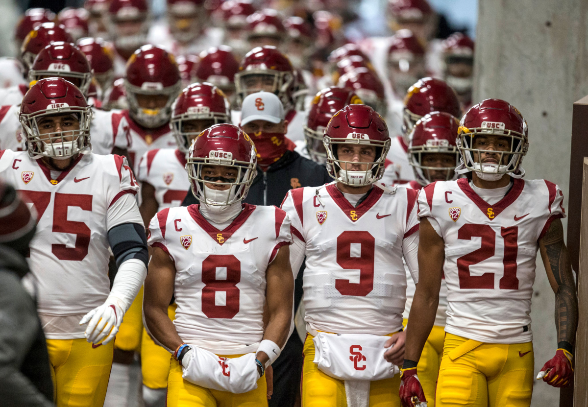 Football players, aligned in rows, walk through a stadium tunnel.