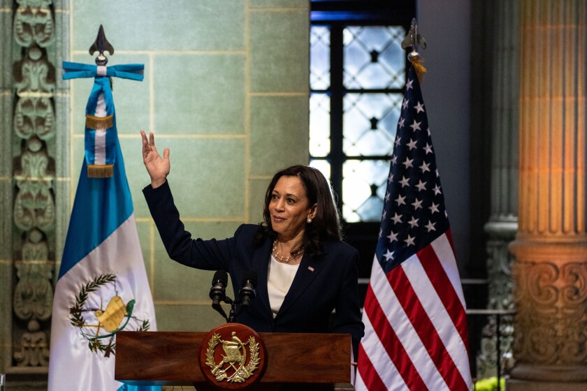 Kamala Harris stands with hands raised between the flags of the United States and Guatemala