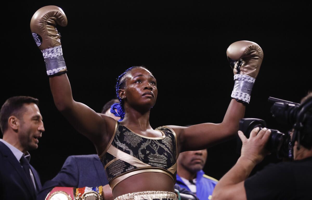 Claressa Shields raises her hands in boxing gloves in the ring.