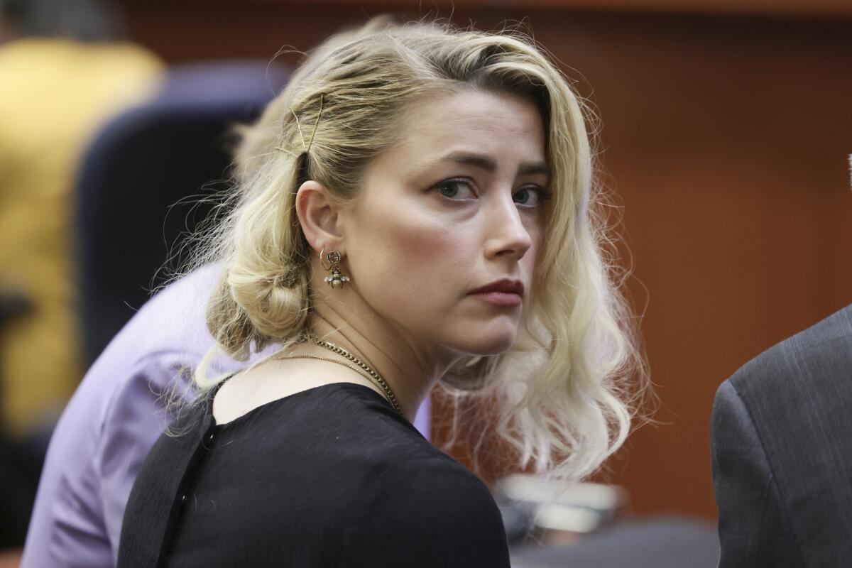 A woman with blond hair wearing black and looking over her shoulder in a courtroom.