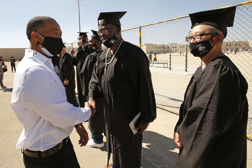LANCASTER, CA - OCTOBER 05: Allen Burnett, 48, left, who had been serving a life sentence for a crime he committed when he was 18 has already crossed the graduation stage at Cal State Los Angeles over the summer, where he graduated Magma Cum Laude more than a year after his release from prison last June, encourages graduates of Cal State LA's Prison B.A. Program before their ceremony inside the California State Prison in Lancaster. A ceremony followed the graduation events for classmates whose sentences were commuted. The program is the first of its kind in California. California State Prison on Tuesday, Oct. 5, 2021 in Lancaster, CA. (Al Seib / Los Angeles Times).