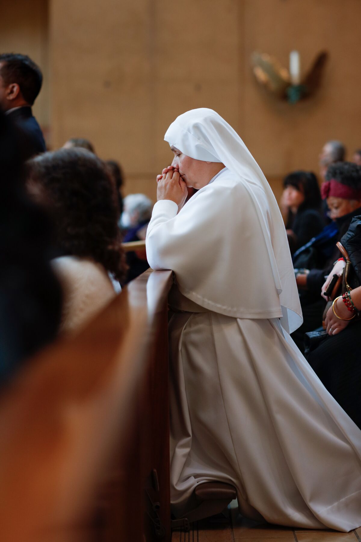 A nun in a white habit prays while kneeling in a church.