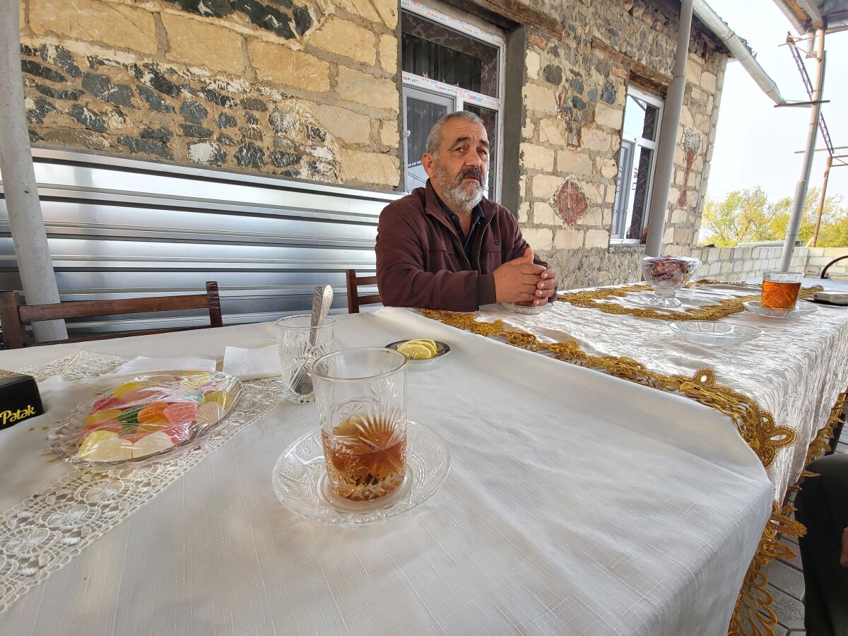 Nizami Aghayev, 56, who lost three members of his family in a missile strike on Ganja, Azerbaijan, sits at a table outdoors.