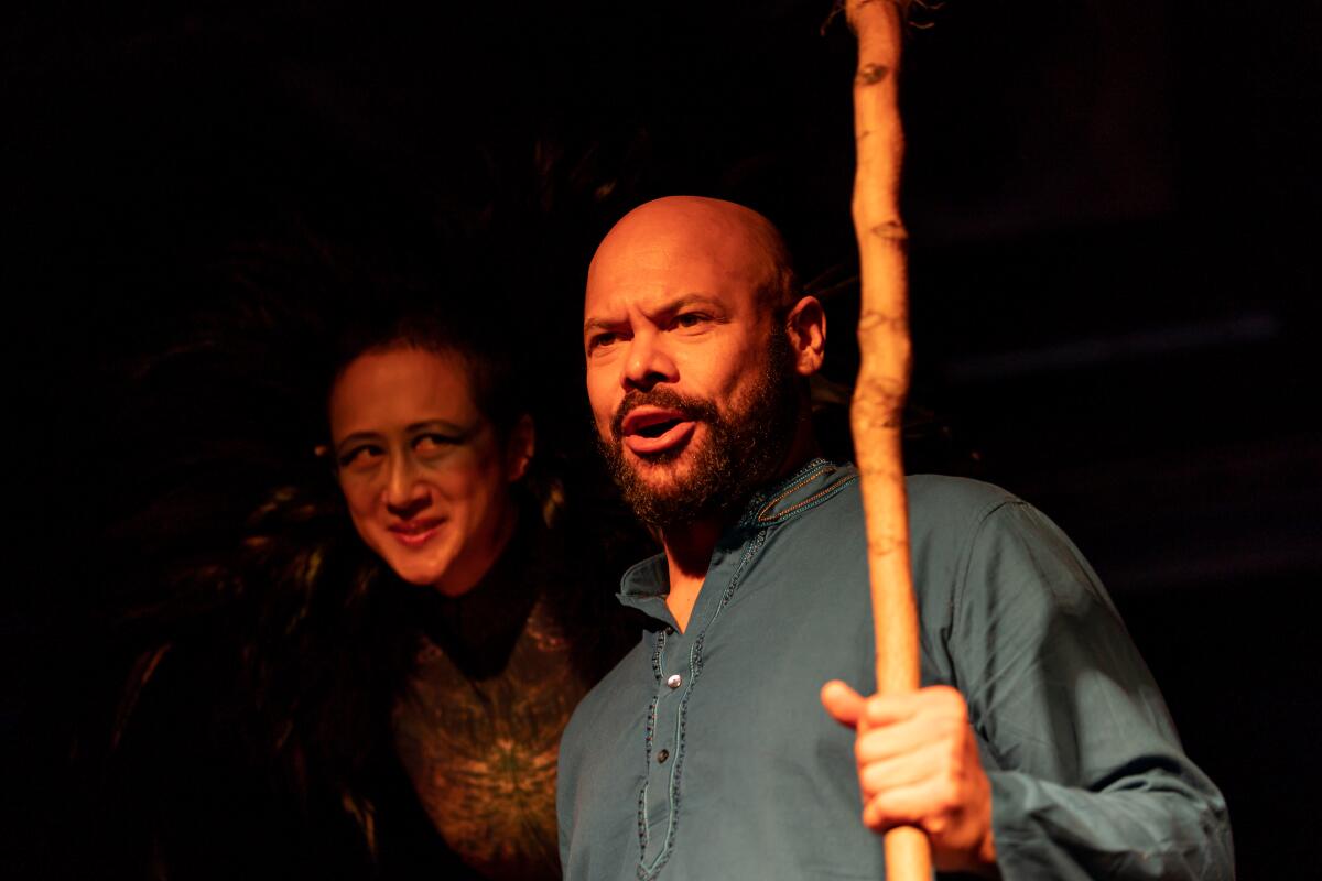 Two actors in a performance of "The Tempest," one holding a staff and the other peering over his shoulder