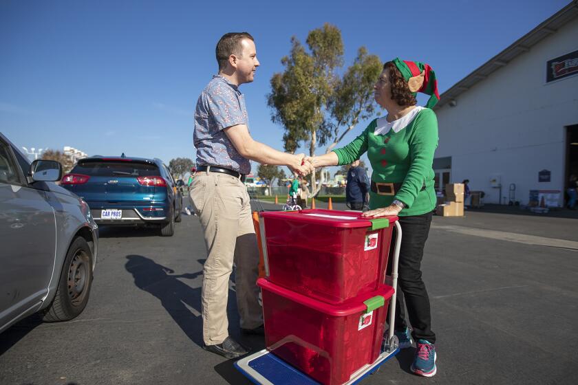 John Corwin of Edwards Lifesciences receives a handshake from Marilyn Smith after dropping off gifts for two families at the Share Our Selves (SOS) annual Adopt A Family Program at the OC Fair & Event Center.