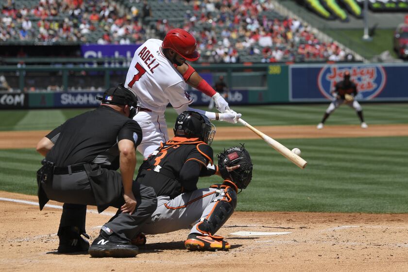 Los Angeles Angels' Jo Adell, center, hits a grand slam as Baltimore Orioles catcher Robinson Chirinos, right, watches along with home plate umpire Mark Carlson during the first inning of a baseball game Sunday, April 24, 2022, in Anaheim, Calif. (AP Photo/Mark J. Terrill)