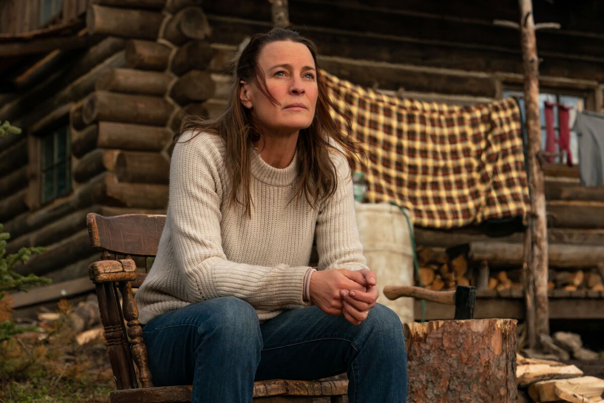 Robin Wright's Edee, in a sweater, sits in a chair outside a cabin.