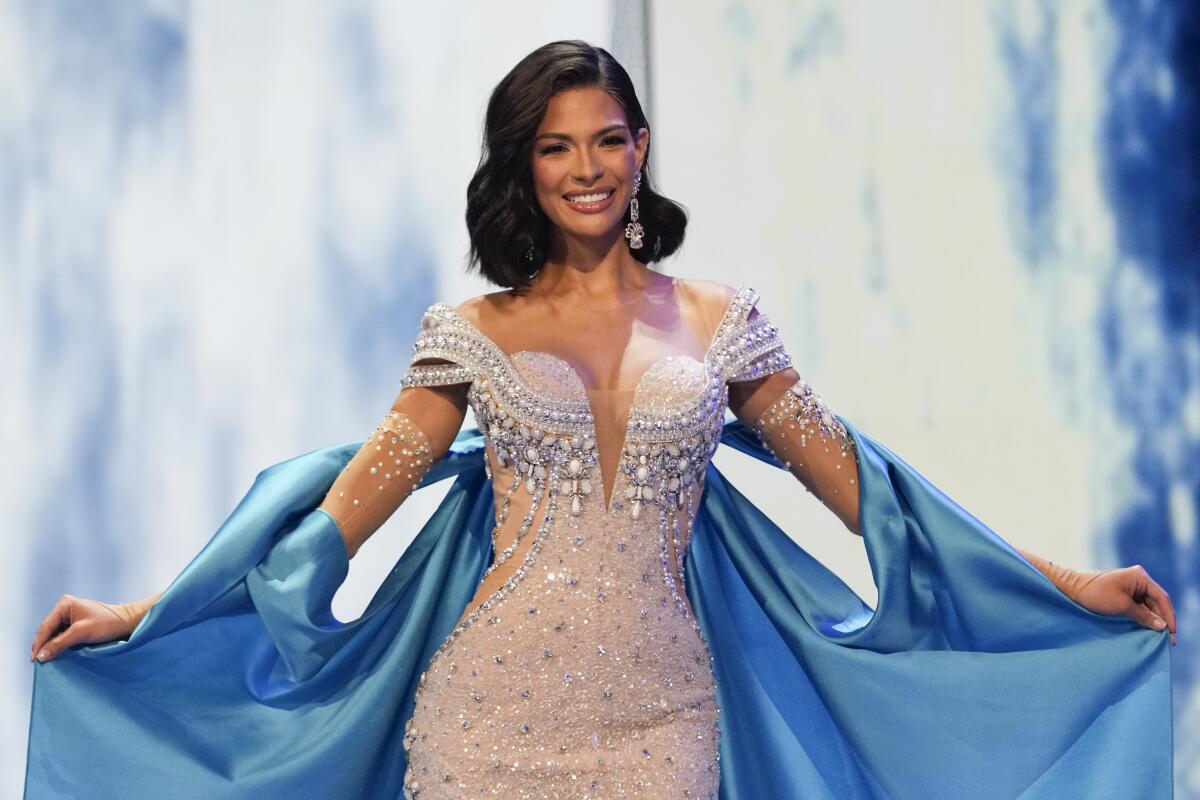 A woman in an evening gown holds out a cape and smiles.