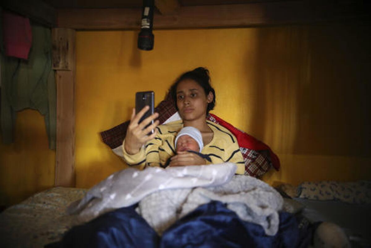 En esta imagen del 12 de junio de 2019, la adolescente migrante Milagro de Jesús Henríquez Ayala, de El Salvador, en la cama con su hijo recién nacido, Alexander, mientras ve Bob Esponja en su celular, en el refugio de la iglesia Ágape Misión Mundial, en Tijuana, México. (AP Foto/Emilio Espejel)