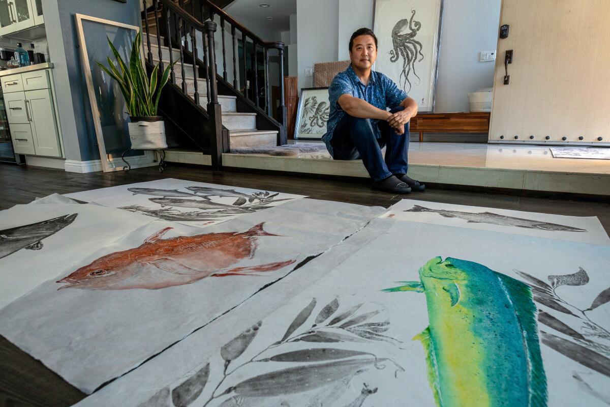 A man sits behind some of his artwork.
