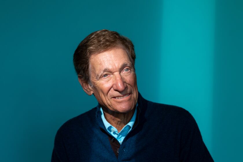 Talk show host Maury Povich poses in a chair before a blue backdrop